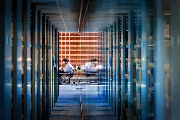 A student sits at a desk at the end of a hallway past dozens of shelves of books in Pius XII Memorial Library.